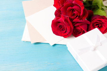Bouquet of red roses White gift box clean sheet, blue wood background. Copy space. Romantic gift for Valentine's Day holiday