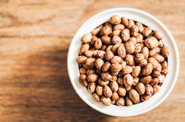 Beans (Phaseolus) in white porcelain bowl on wooden background, vegetarian concept.