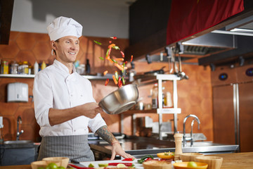 Waist up portrait of handsome professional chef cooking in restaurant kitchen and mixing vegetables in pot, copy space