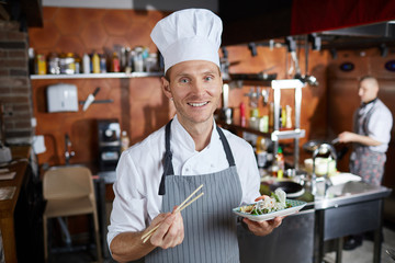 Waist up portrait of professional Asian food chef smiling at camera while posing in restaurant kitchen, copy space