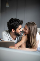 Happy young couple looking a tablet together and laughing while lying on the bed