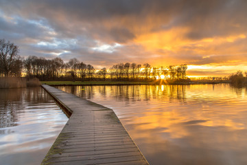 Fototapeta premium Wooden walkway in lake under orange sunset
