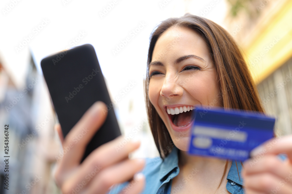 Poster Excited woman paying online with credit card and cellphone