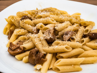 Italian cuisine, tasty short pasta dish with porcini mushrooms cheese and black pepper on wooden table outdoors for true epicureans