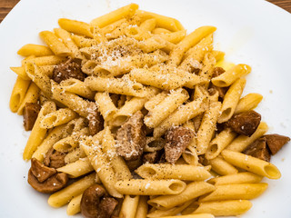 Italian cuisine, tasty short pasta dish with porcini mushrooms cheese and black pepper on wooden table outdoors for true epicureans