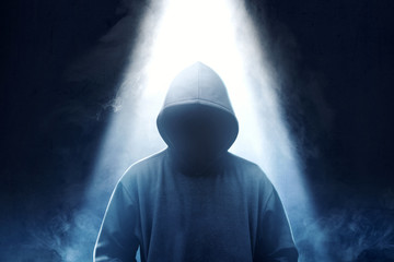 Hacker in black hoodie standing with smoke and light from the top