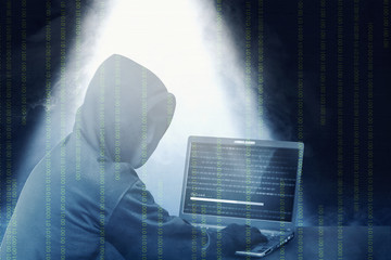 Hacker in black hoodie using laptop on the desk to hacking system with binary code and upload the...