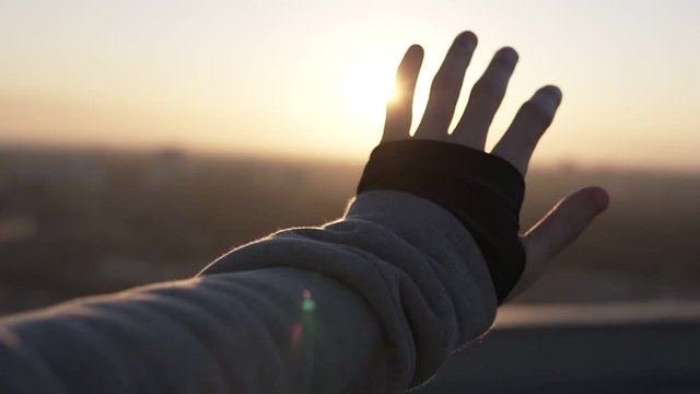 Man hand touching the sunlight by hand over beautiful sky background while standing on the roof. Happy man looking at sunrising through his fingers. Slow motion
