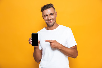 Image of optimistic man 30s in white t-shirt smiling and holding cell phone while standing isolated