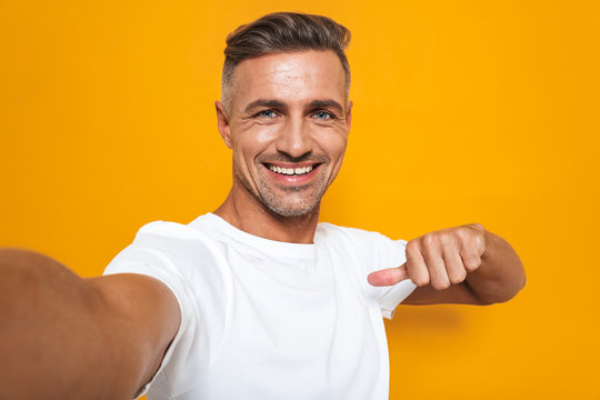 Image of bearded man 30s in white t-shirt smiling and taking selfie photo