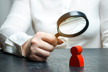 Business woman examines a red man's figure through a magnifying glass. Analysis of the personal qualities of the employee. Characteristic. Unreliable employee. Toxicity in the staff of workers