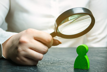 Businesswoman is holding a magnifying glass over a green man figure. Search for a talented employee. Identifying strengths in the company. Disclosure skills. Employee characteristics