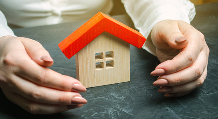 A woman is protecting a miniature wooden house with a red roof. Property insurance concept. Protection of housing. Security and safety family and life. Insurance agent services. Support
