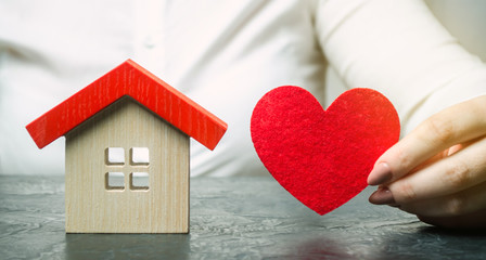 A woman holds a red heart near the wooden house. Insurance agent services. Property insurance...