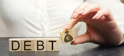 A hand puts a wooden block with a euro image and the word Debt. Payment of taxes and of debt to the...
