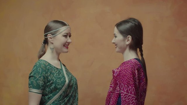 Close-up of beautiful females in indian sari with bindi points, tika decorations joining hands in namaste greeting at friendly home meeting. Happy to see each other women expressing mutual respect.