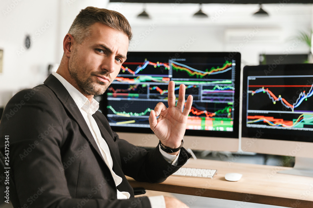 Canvas Prints image of unshaved businessman working in office on computer with graphics and charts at screen