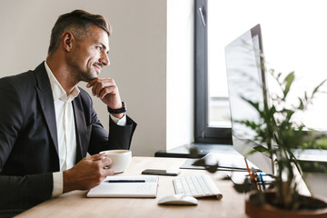 Obraz premium Image of unshaved businessman drinking coffee while working on computer in office