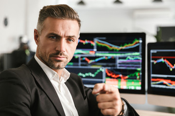 Image of businesslike man working in office on computer with graphics and charts at screen