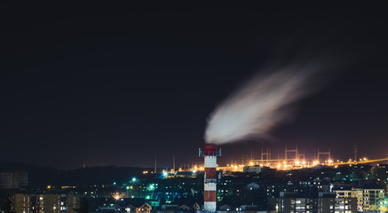 Chimney of a heating plant releasing smoke above the city at night