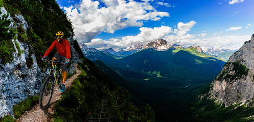 Tourist cycling in Cortina d'Ampezzo, stunning rocky mountains on the background. Man riding MTB enduro flow trail. South Tyrol province of Italy, Dolomites.