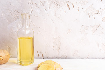 Small glass bottle of ginger oil on white table on light background. 