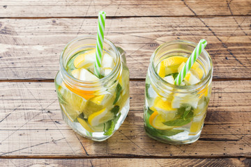 Lemonade drink of soda water, lemon and mint leaves in jar on wooden background.