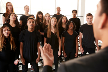 Male And Female Students Singing In Choir With Teacher At Performing Arts School