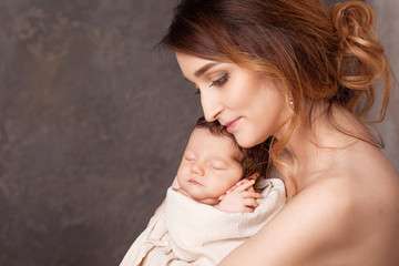 Pretty young woman holding a newborn baby in her arms. Portrait of mother and little baby. Happy family concept. Copy space