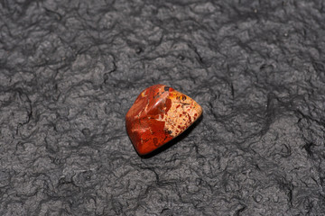 Carneol gem isolated on black stone background. Macro shot.