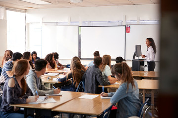 Female High School Teacher Standing By Interactive Whiteboard Teaching Lesson