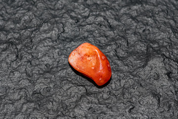 Carneol gem isolated on black stone background. Macro shot.