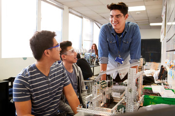 Teacher With Two Male College Students Building Machine In Science Robotics Or Engineering Class
