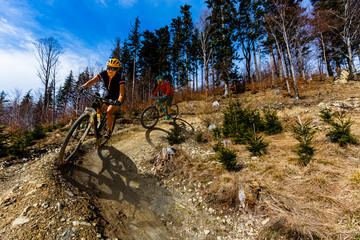 Cycling woman and men riding on bikes at sunset mountains forest landscape. Couple cycling MTB enduro flow trail track. Outdoor sport activity.