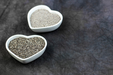 Black and white chia seeds in small heart shapped ceramic bowls on a dark rustic background