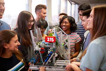 College Students With Teacher Holding Machine In Science Or Robotics Class
