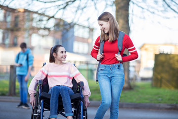 Teenage Girl In Wheelchair Talking With Friend As They Leave High School