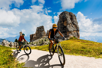 Cycling woman and man riding on bikes in Dolomites mountains landscape. Couple cycling MTB enduro trail track. Outdoor sport activity.