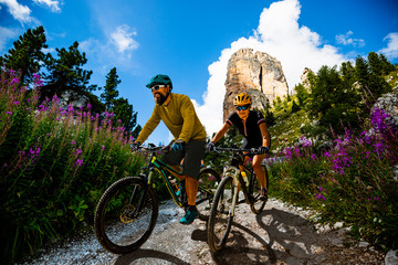 Cycling woman and man riding on bikes in Dolomites mountains landscape. Couple cycling MTB enduro...