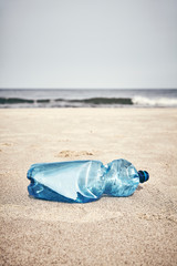 Empty plastic bottle on a beach, selective focus, color toning applied.