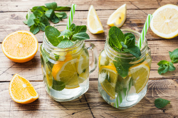 Lemonade drink of soda water, lemon and mint leaves in jar on wooden background.