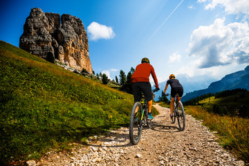 Cycling woman and man riding on bikes in Dolomites mountains landscape. Couple cycling MTB enduro trail track. Outdoor sport activity.