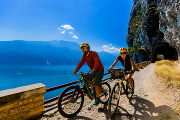 Cycling woman and man riding on bikes at sunrise mountains and Garda lake landscape. Couple cycling MTB enduro flow sentiero ponale trail track. Outdoor sport activity.