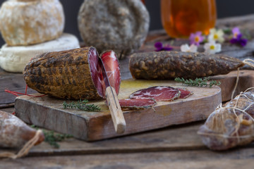 Several variety of traditional Corsican charcuterie with an olive branch and black olives on wooden...