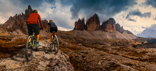 Cycling woman and man riding on bikes in Dolomites mountains andscape. Couple cycling MTB enduro trail track. Outdoor sport activity.
