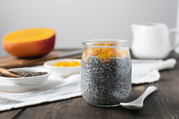 Chia pudding in glass jar with almond milk and mango on rustic wooden table