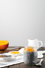 Chia pudding in glass jar with almond milk and mango on rustic wooden table