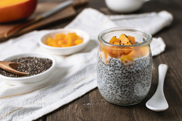 Chia pudding in glass jar with almond milk and mango on rustic wooden background