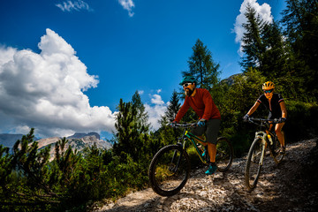 Cycling woman and man riding on bikes in Dolomites mountains andscape. Couple cycling MTB enduro trail track. Outdoor sport activity.