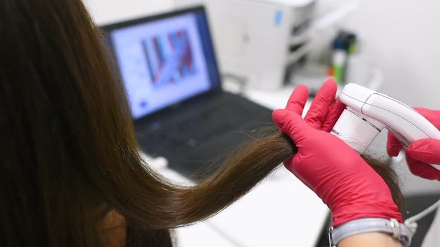 doctor dermatologist diagnoses the structure of the hair of a young pretty girl with a special tool - a trichoscope. Trichology, trichogram